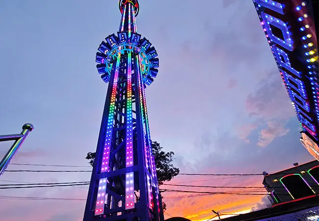 Beston Drop Tower Illuminated with Colorful LED Lights Against a Sunset Sky in Russia